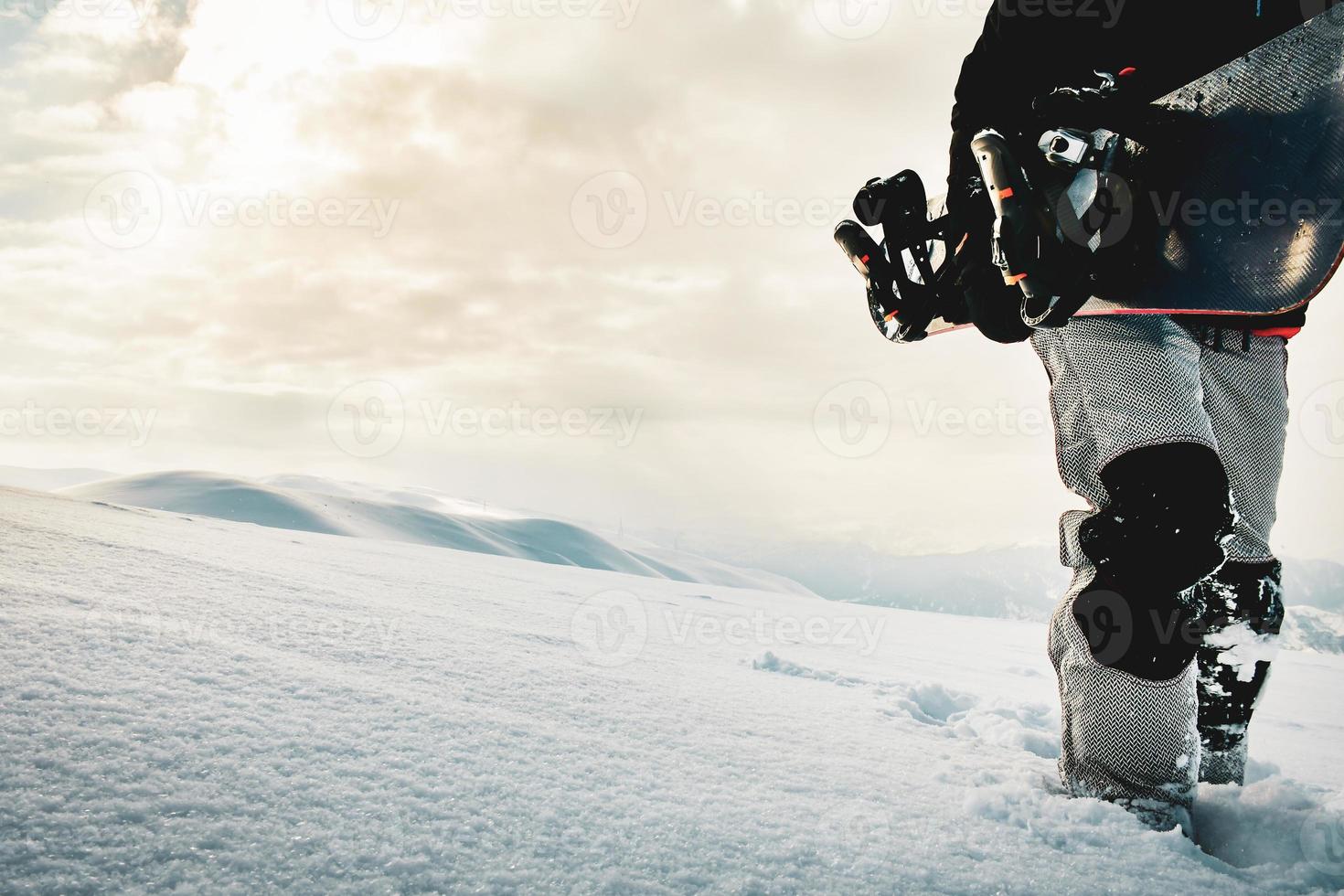 Snowboarder dressed in a full protective gear for extreme freeride snowboarding posing with a snowboard walking. Isolated on gray white snow background. photo