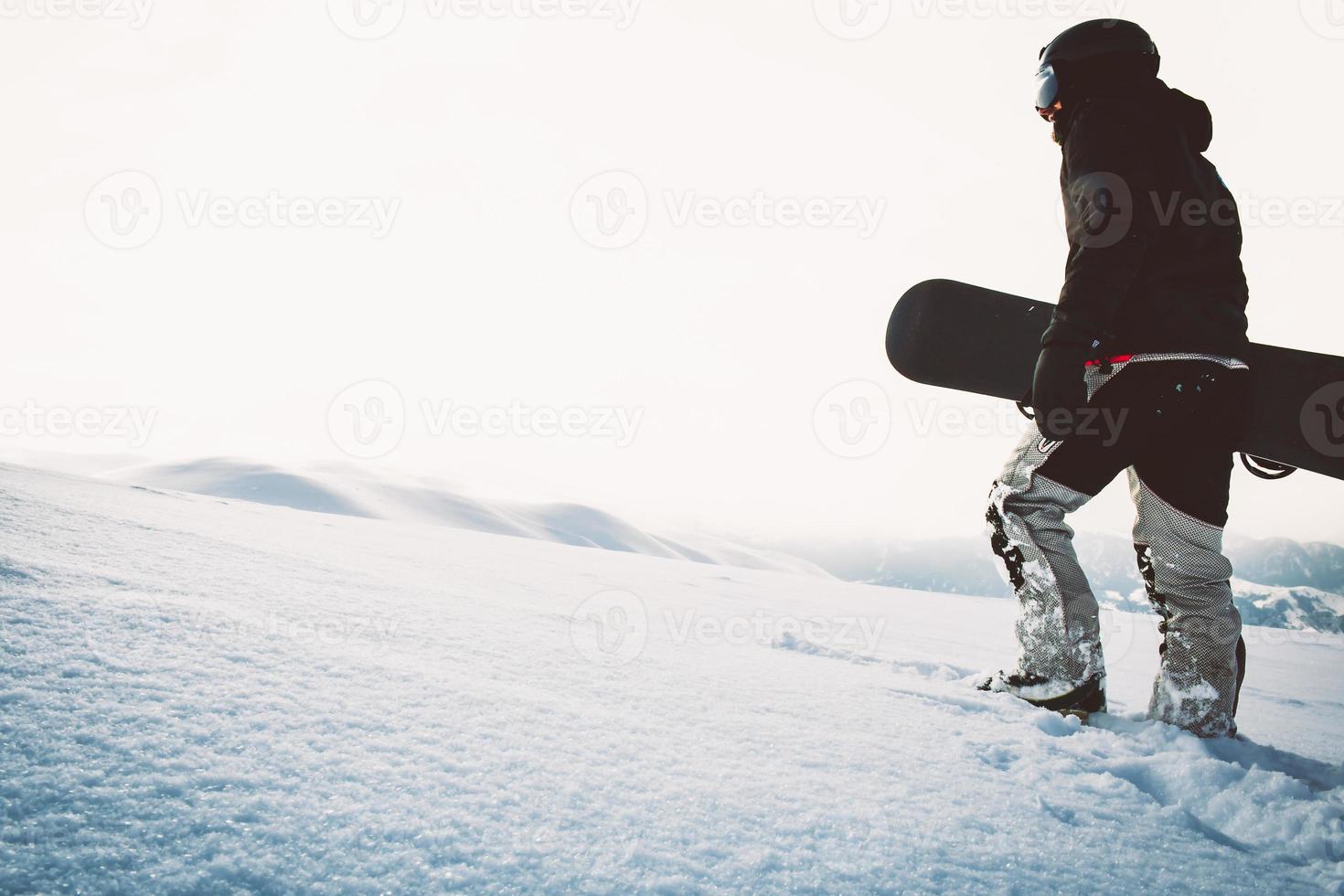 Snowboarder walking with snowboard during sunset in the snowy mountains. Cinematic solo freerider snowboarder background photo