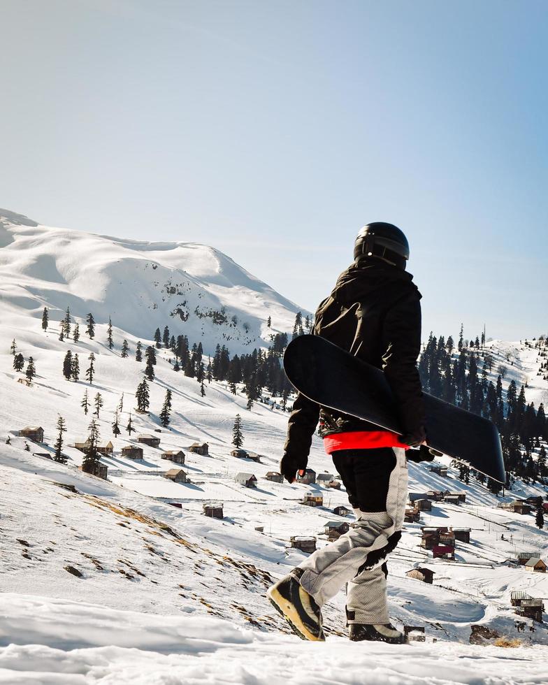 Snowboarder dressed in a full protective gear for extreme freeride snowboarding posing with a snowboard walking. Isolated on gray white snow background. photo