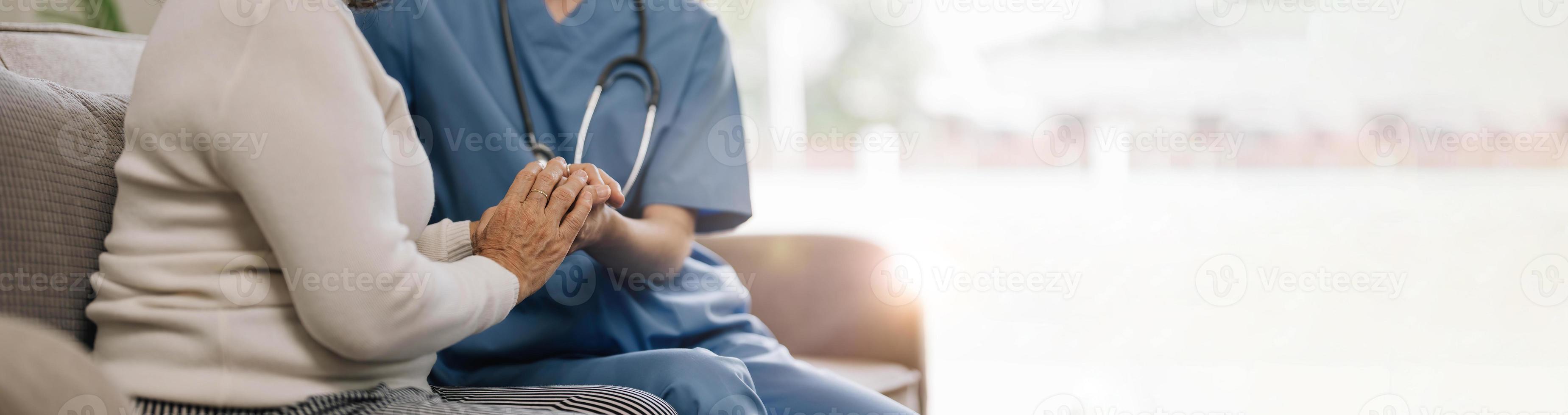 Happy patient is holding caregiver for a hand while spending time together. Elderly woman in nursing home and nurse. photo