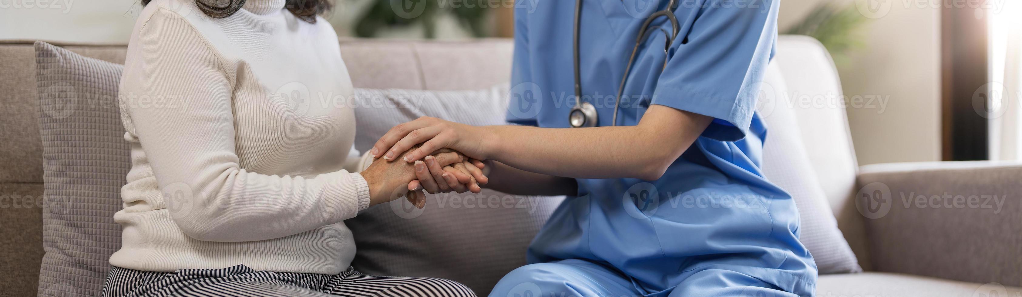 Happy patient is holding caregiver for a hand while spending time together. Elderly woman in nursing home and nurse. photo