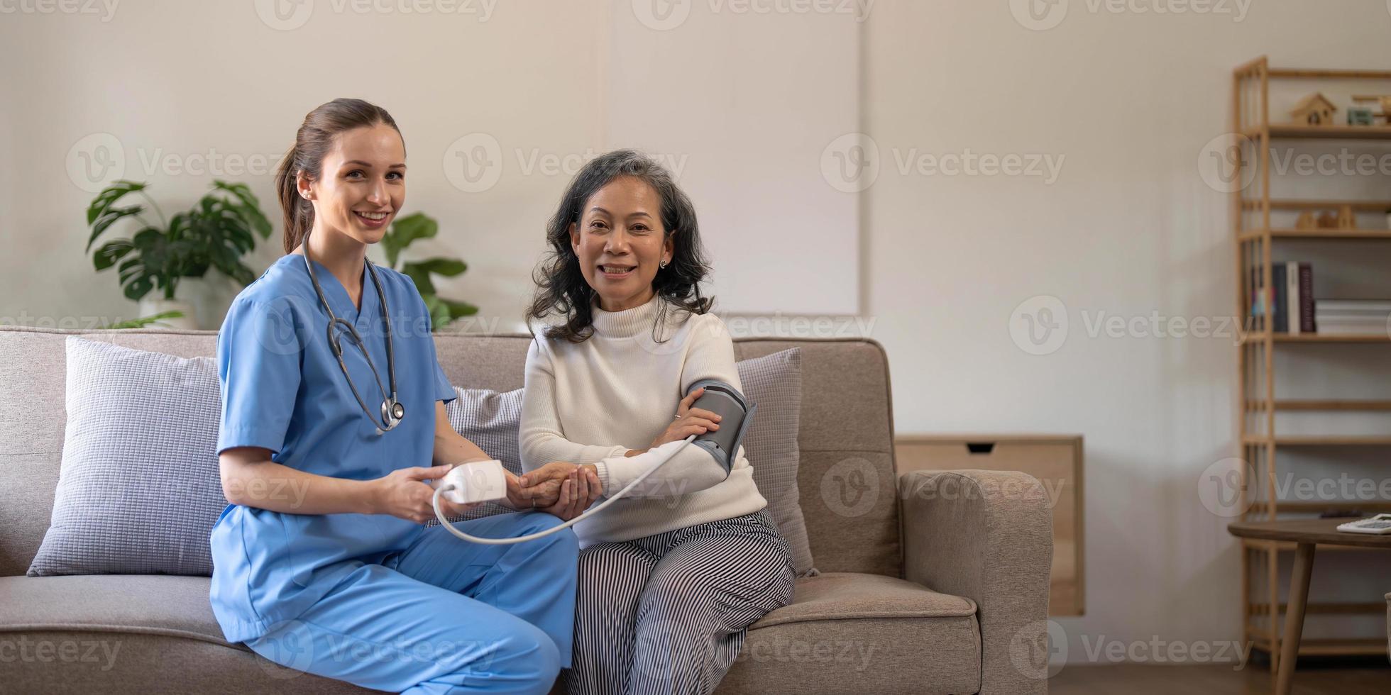 feliz mujer mayor que su cuidadora le mide la presión arterial en un asilo de ancianos. enfermera feliz midiendo la presión sanguínea de una anciana en la sala de estar foto