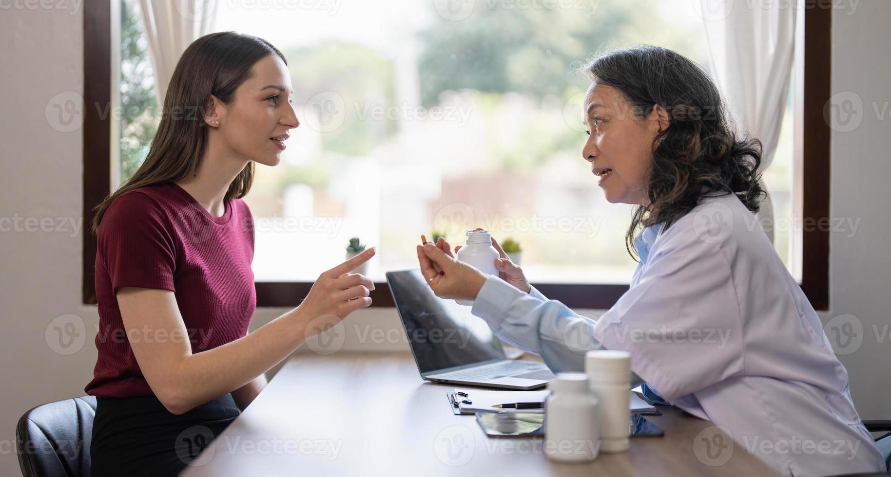 Middle aged female pediatrician listening to young woman's complaints with health problems And write down on the medical history paper during the treatment. health concept photo