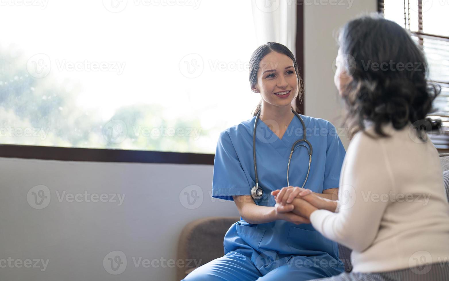 Happy patient is holding caregiver for a hand while spending time together. Elderly woman in nursing home and nurse. Aged elegant woman and tea time at nursing home photo
