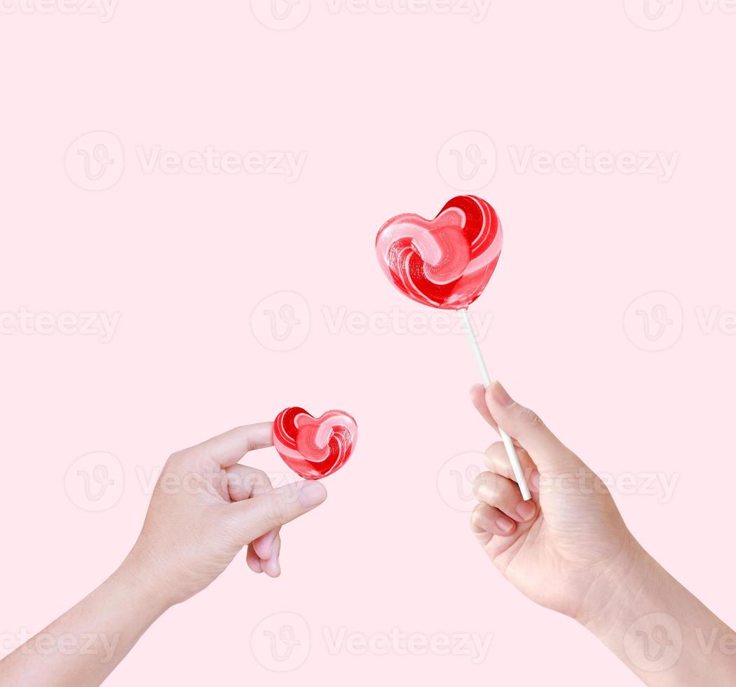 Heart shaped lollipop candy in hand isolated on pink background. photo