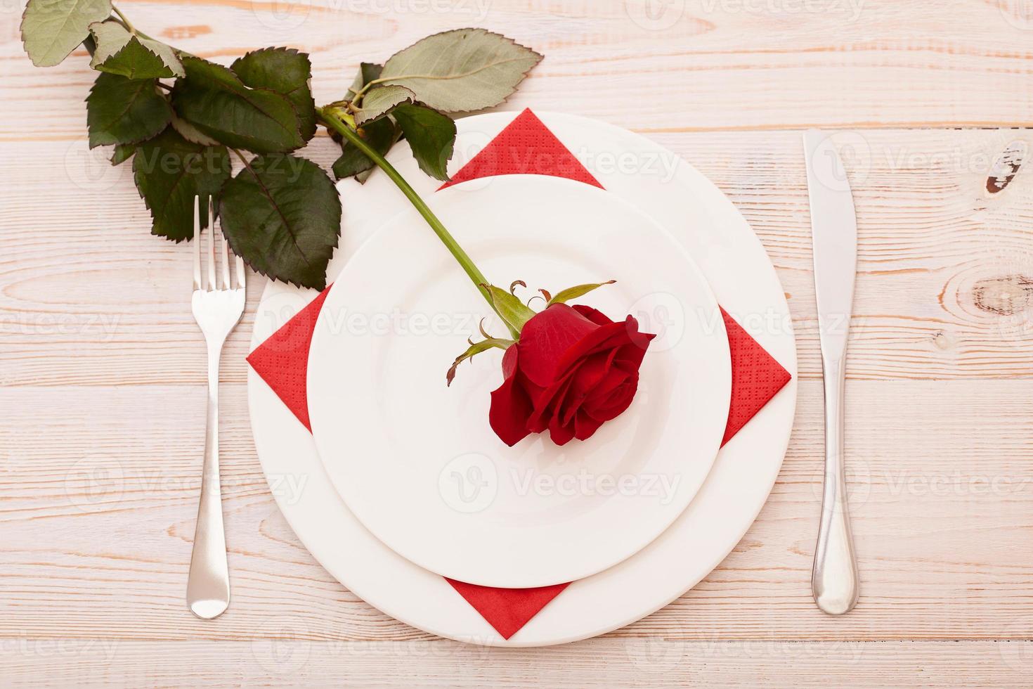 Top view of tableware of round and heart shaped empty plate, metal knife and fork served on white wooden table with glowing candle and gift box prepared for celebration of saint valentine day photo