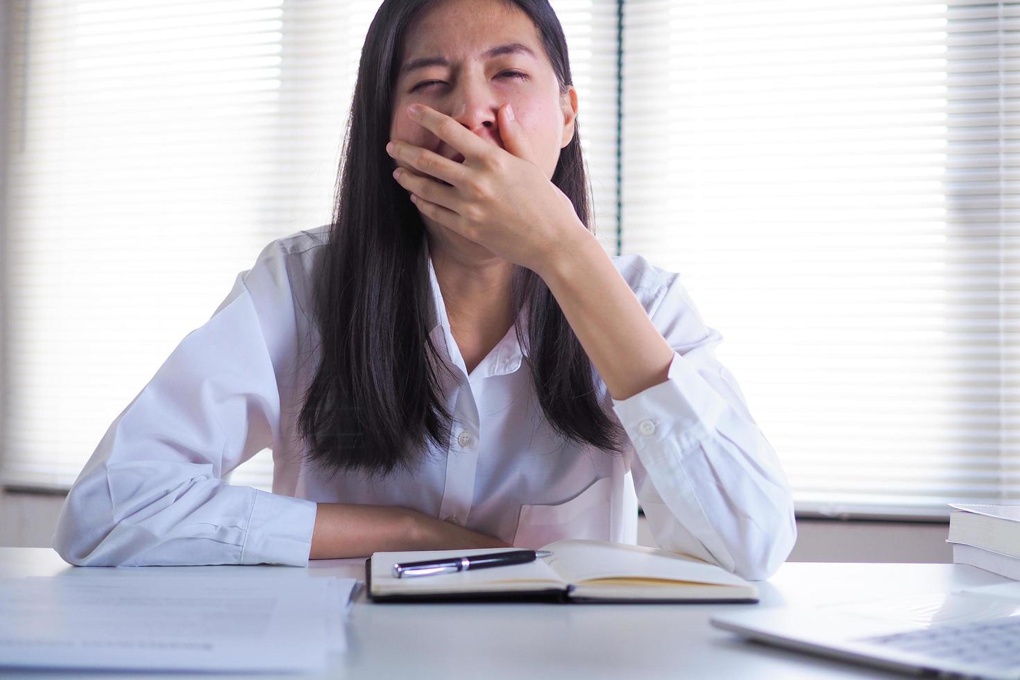 Asian businesswoman yawns and sleepy while working and researching at the office. photo