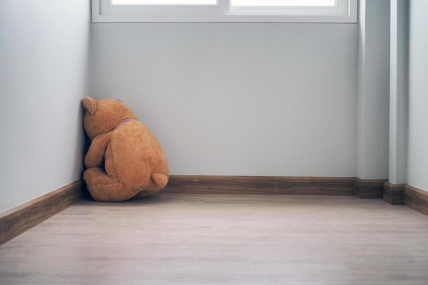 concepto infantil de tristeza. el oso de peluche sentado solo contra la pared de la casa, se ve triste y decepcionado. foto