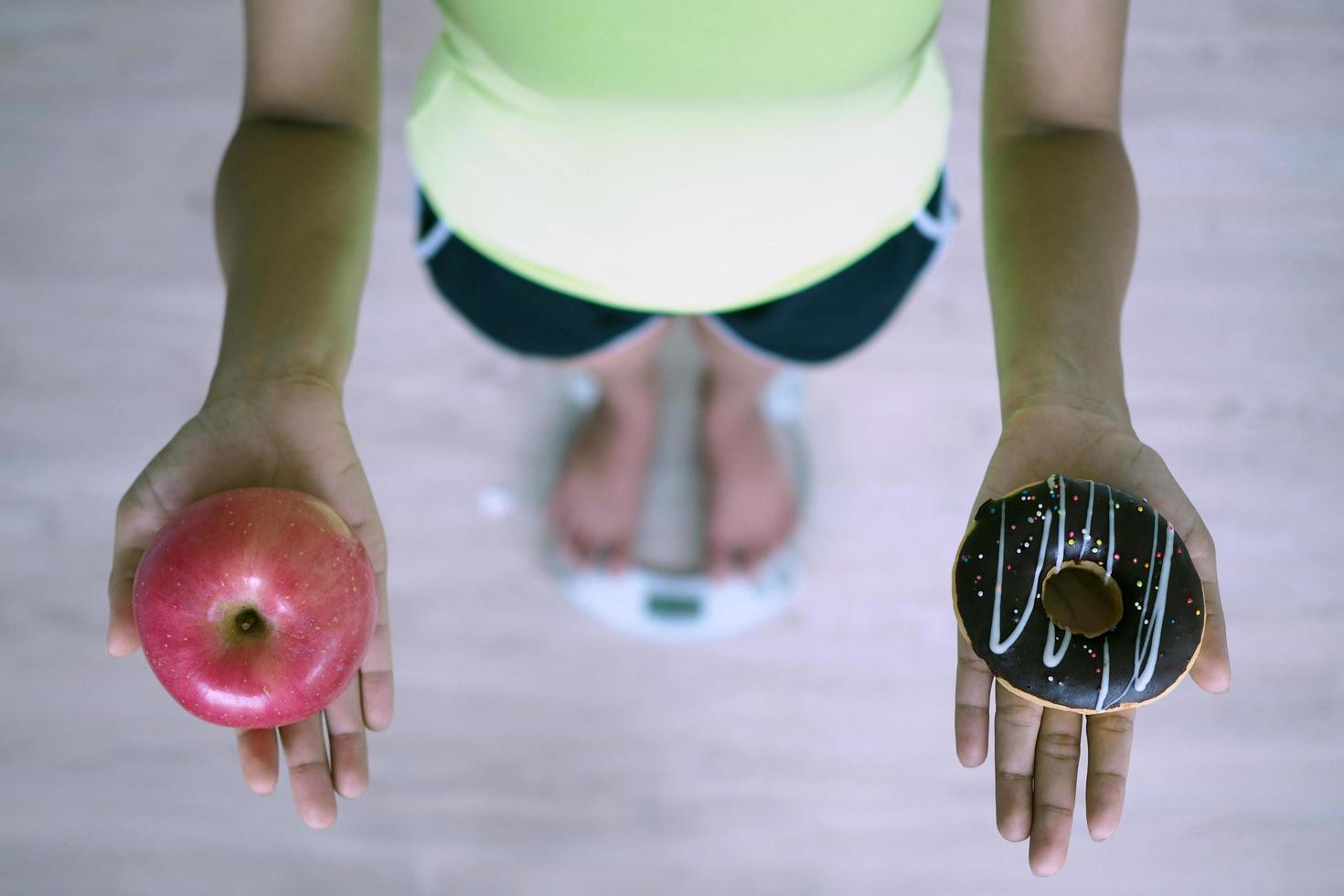 Women are weighing with scales, holding apples and donut. The decision to choose junk food that is not good for health and fruits that are high in vitamin C is good for the body. Diet concept photo