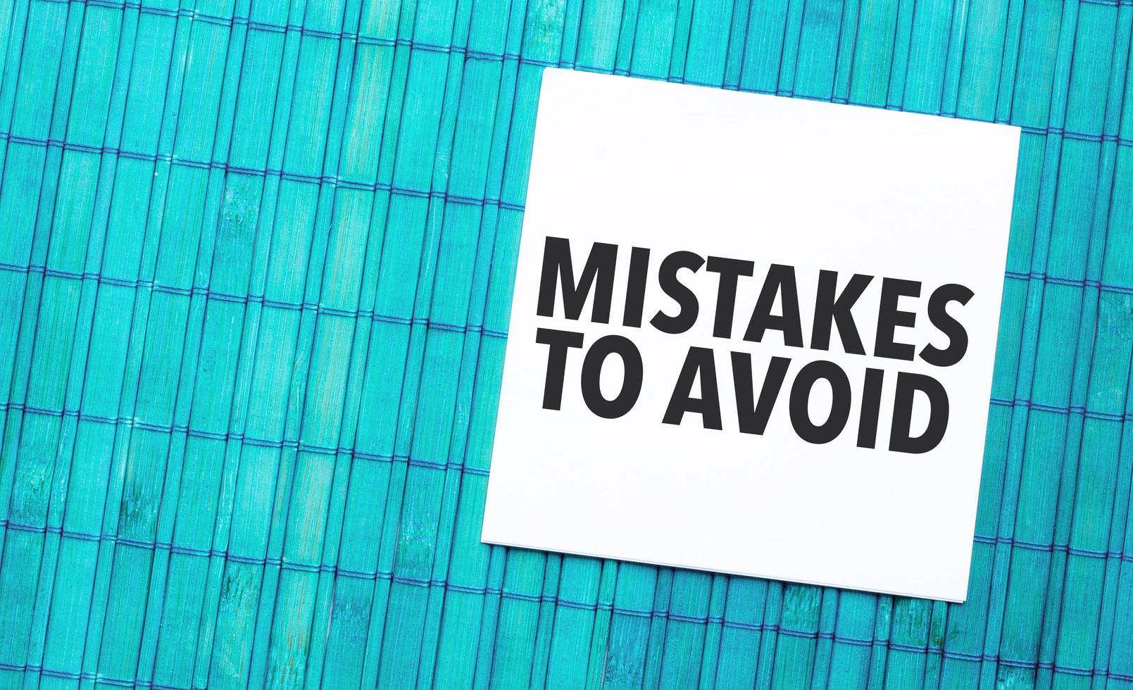 Mistakes To Avoid word on torn paper with blue wooden background photo