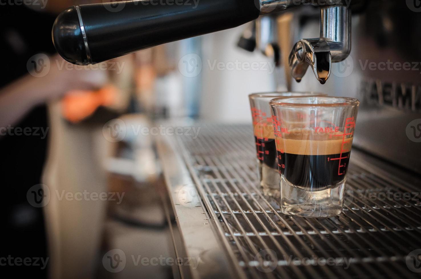 Primer plano de café negro en la taza medidora puesta en la cafetera, máquina de café haciendo espresso foto