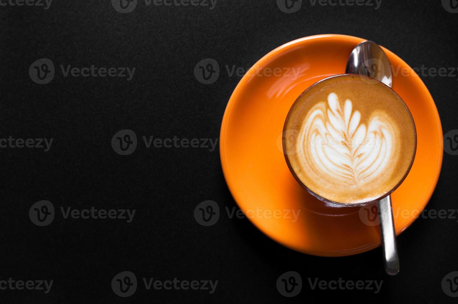 Hot latte in orange cup with floral pattern in foam on a dark background photo