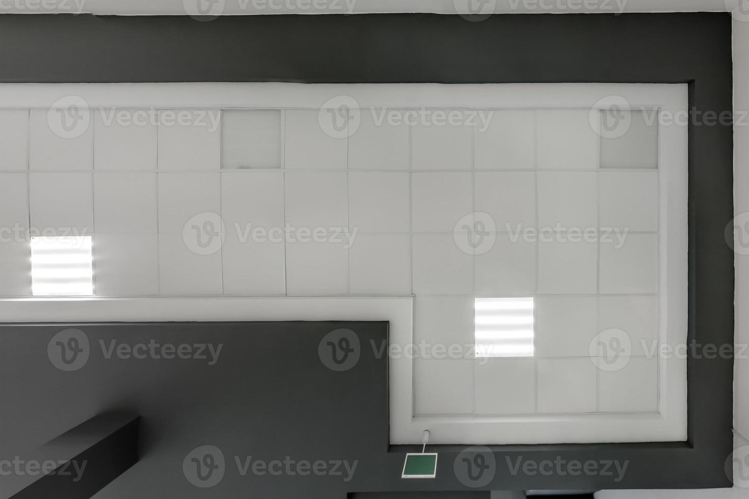 cassette stretched or suspended ceiling with square halogen spots lamps and drywall construction in empty room in house or office with column. Looking up view photo