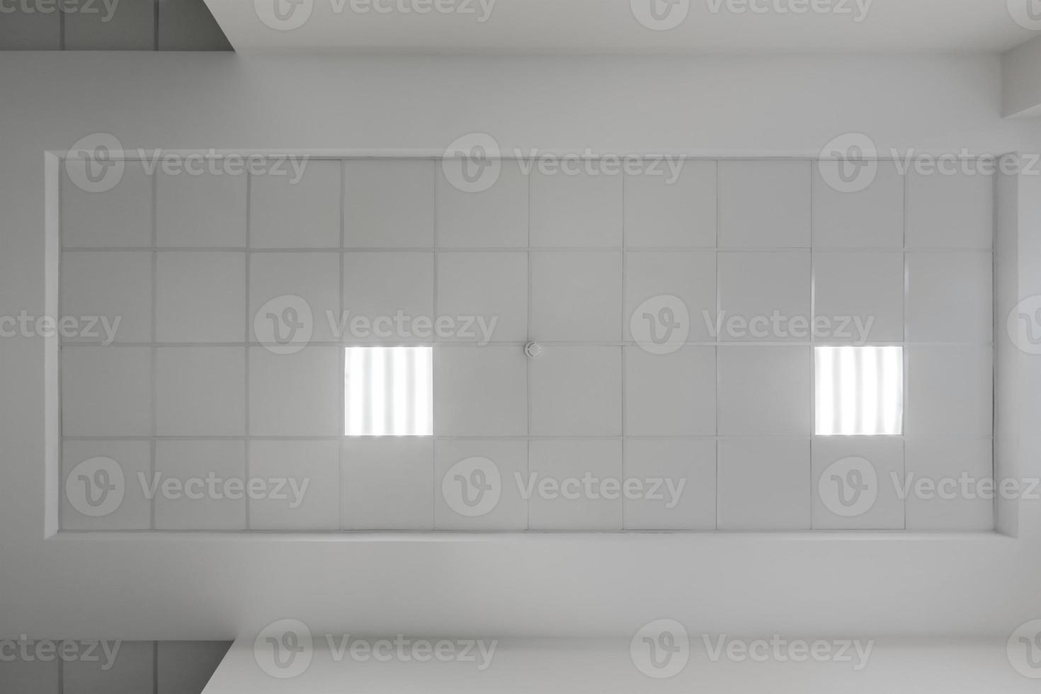 cassette stretched or suspended ceiling with square halogen spots lamps and drywall construction in empty room in house or office with column. Looking up view photo