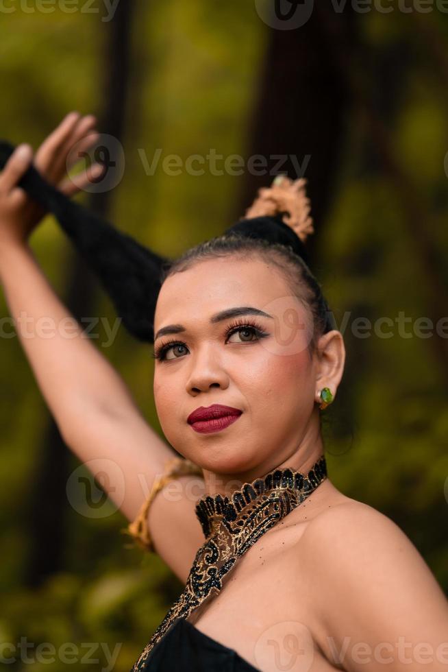 Asian woman holding her black hair in a green costume while wearing makeup and posing in front of the forest during the dance festival photo