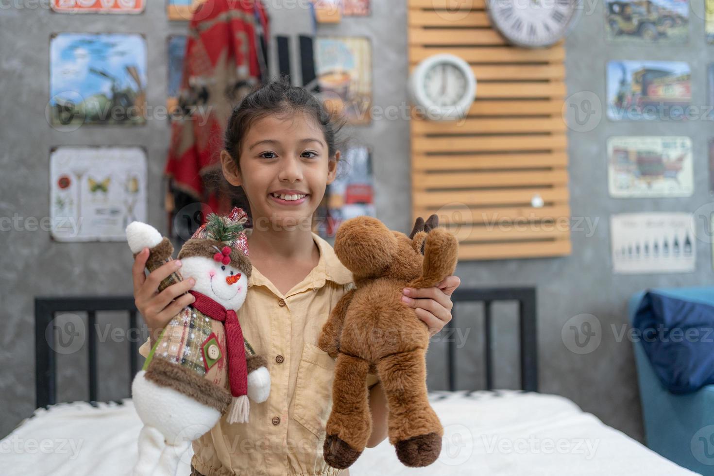 Sweet little girl is hugging a teddy bear, looking at camera and smiling while sitting on her bed at home. photo