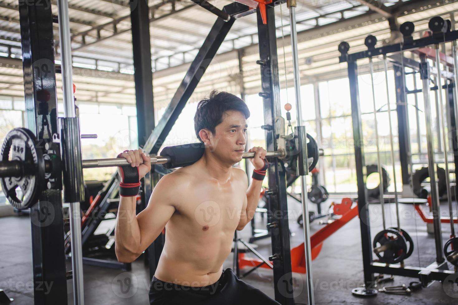 Man doing squat exercises with a barbell in gym photo
