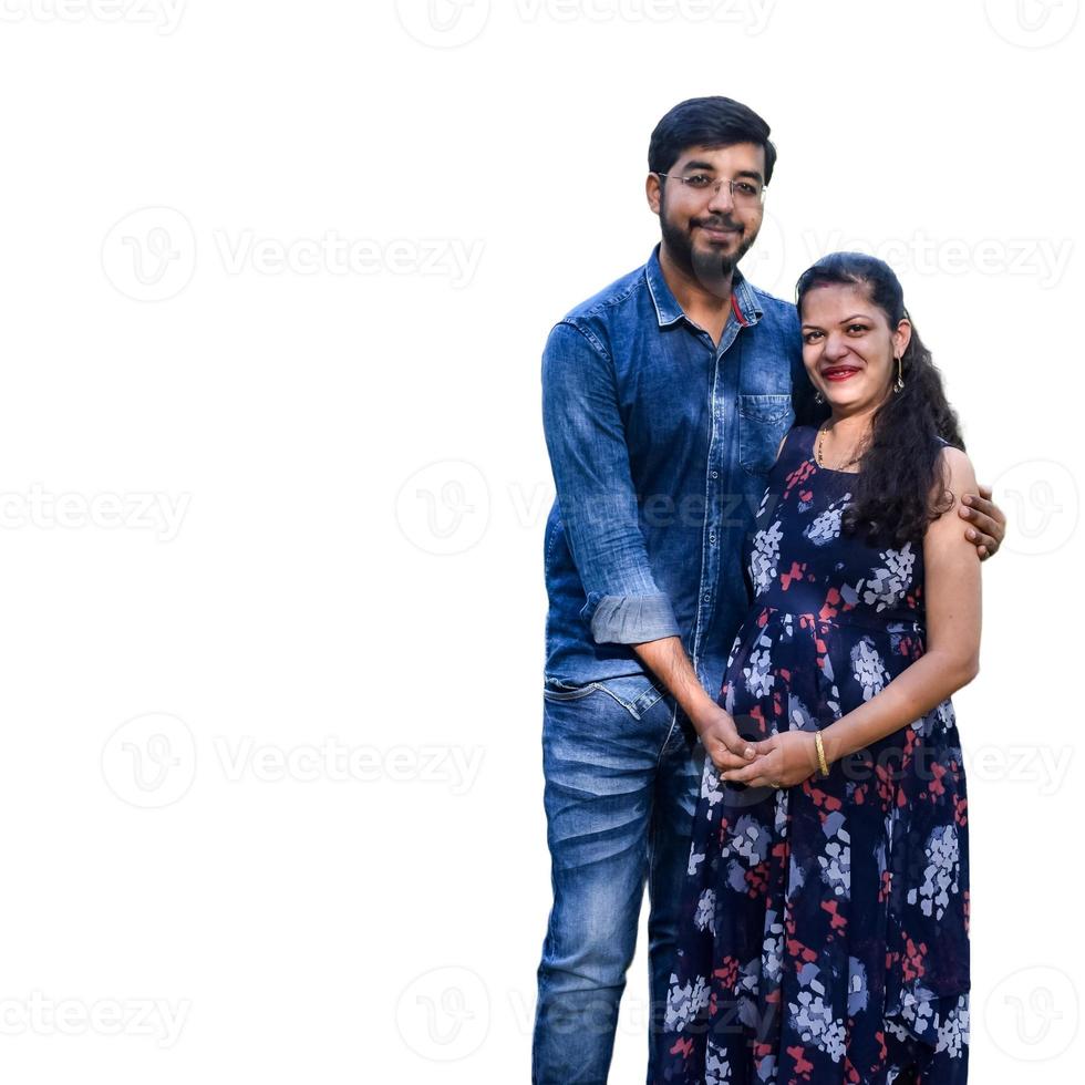 Indian couple posing for maternity baby shoot with white plain background. The couple is posing in a lawn with green grass and the woman is falunting her baby bump in Lodhi Garden in New Delhi, India photo