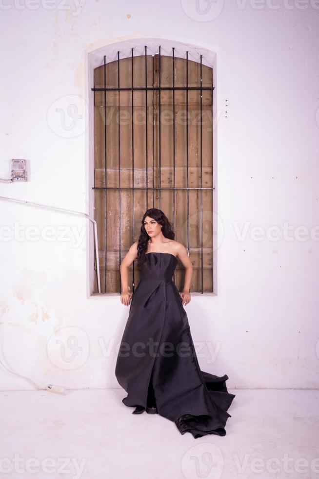 mujer elegante con un vestido negro parada frente a la ventana rústica de madera foto