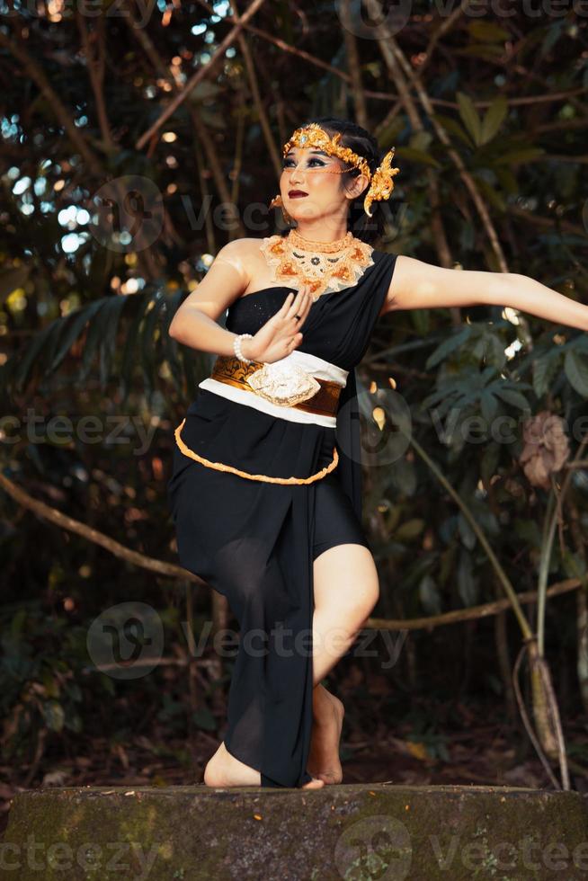 Balinese woman dancing on the top of the rock while wearing a black costume and a golden crown on her head photo