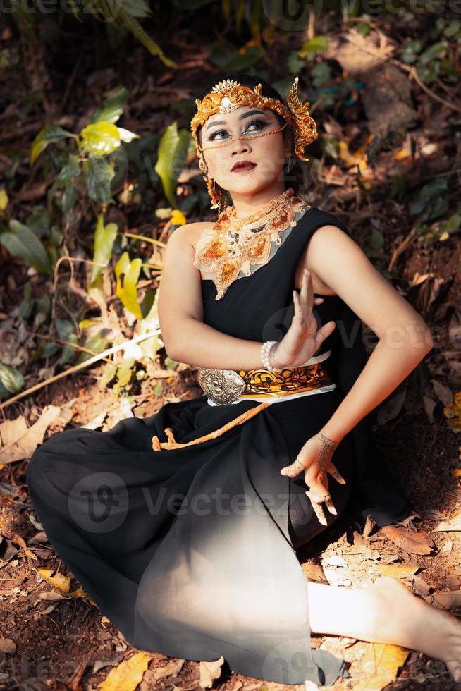 Indian woman sitting with a black dress and makeup on her face while wearing a golden crown and golden necklace on her body photo