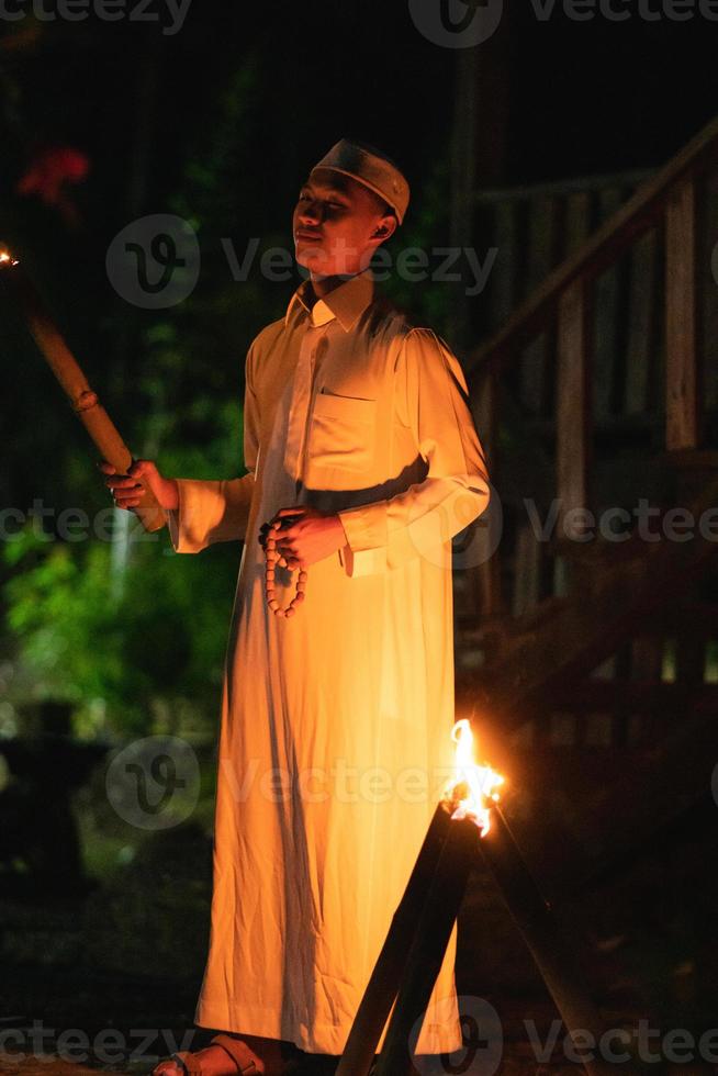 A Muslim man standing with the fire torch in her hand at the front of the village photo