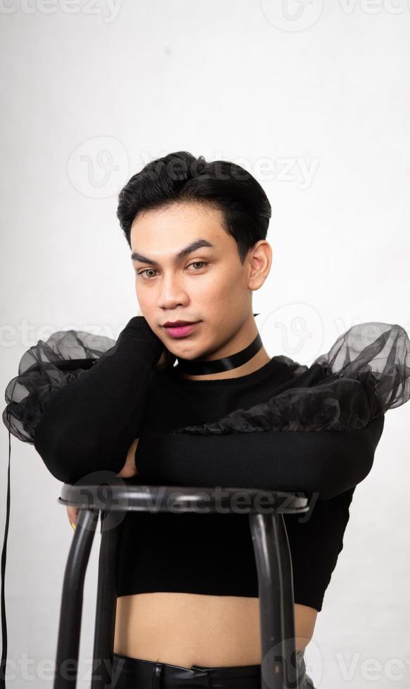 beautiful Asian man posing with the chair while wearing a black costume and makeup photo