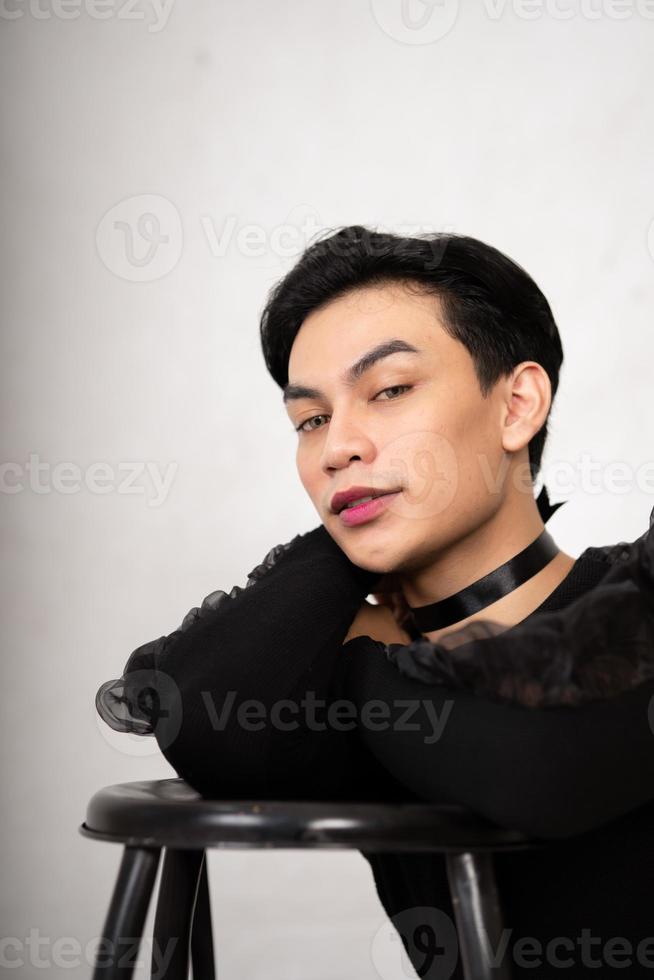 beautiful Asian man posing with the chair while wearing a black costume and makeup photo