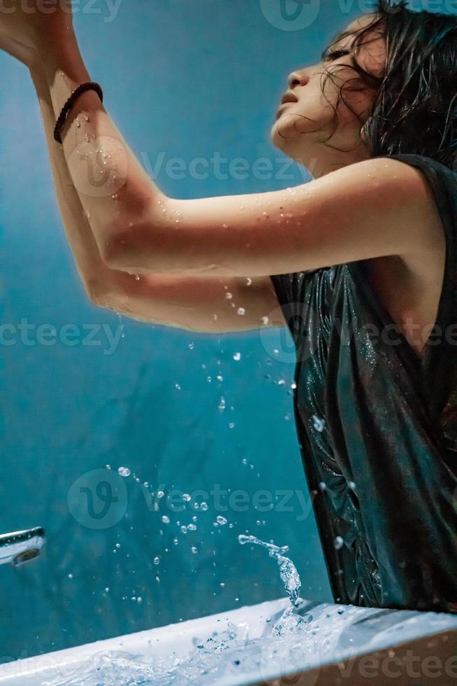 chica de la ciudad que hace fluir el agua a la mano desde el lavabo mientras se baña en el baño foto