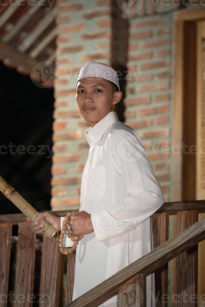 A Muslim man standing on the stairs in front of the traditional house photo