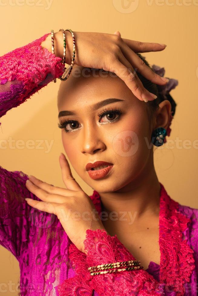 hermosa mujer balinesa maquillada con un vestido rosa mientras posa con manos exóticas foto