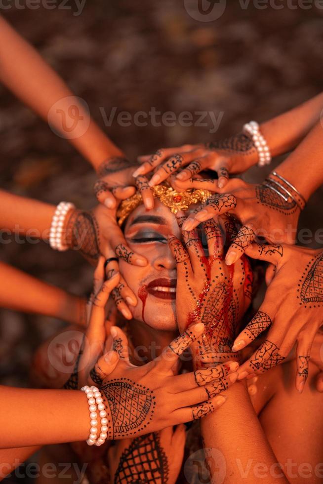 A Lot of hands holding an Asian man's face who had fake blood on her red lips like he was in pain photo