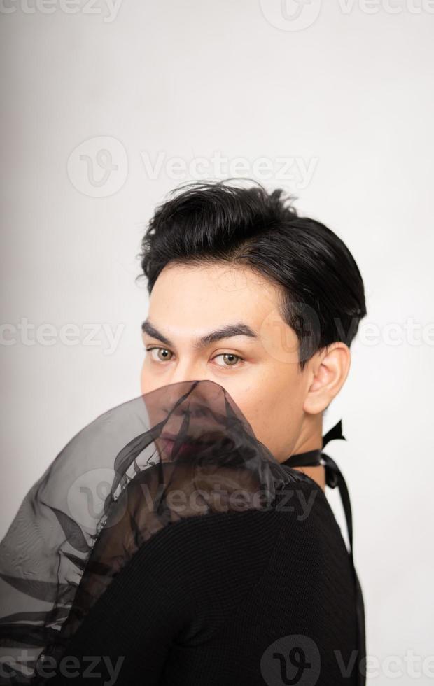 Asian man poses in a black costume while wearing makeup and black hair photo