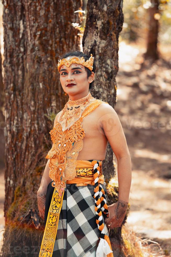 Balinese man standing in the forest while wearing a gold crown and golden necklace photo