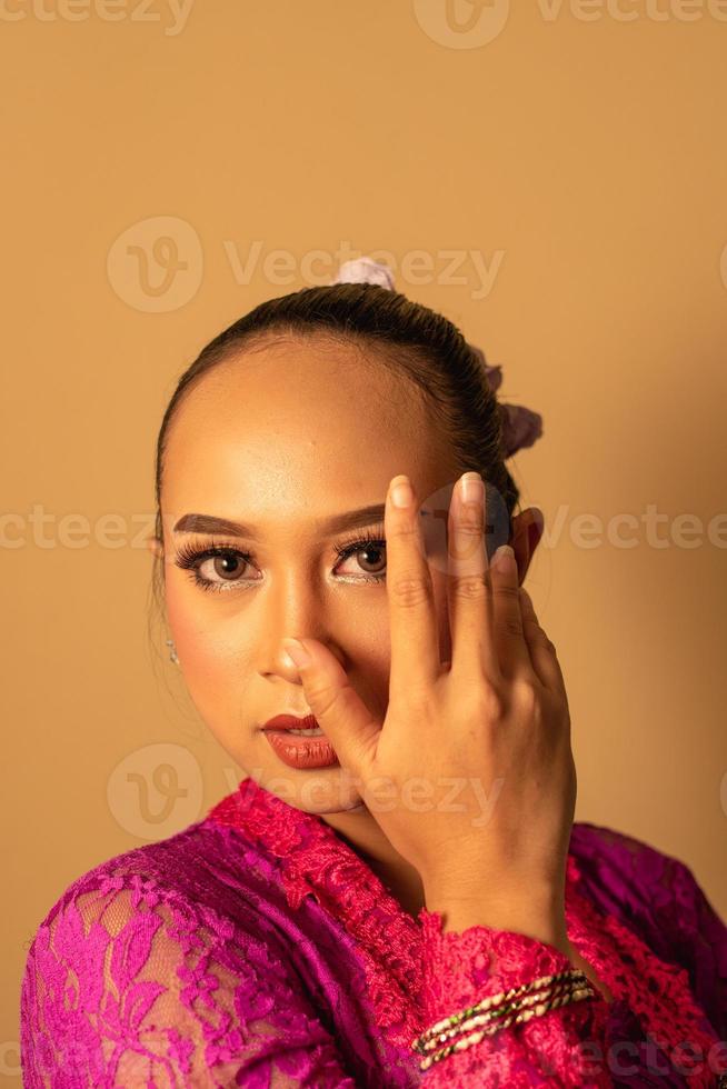 Portrait of Balinese woman with pink dress pose with hands on the face photo