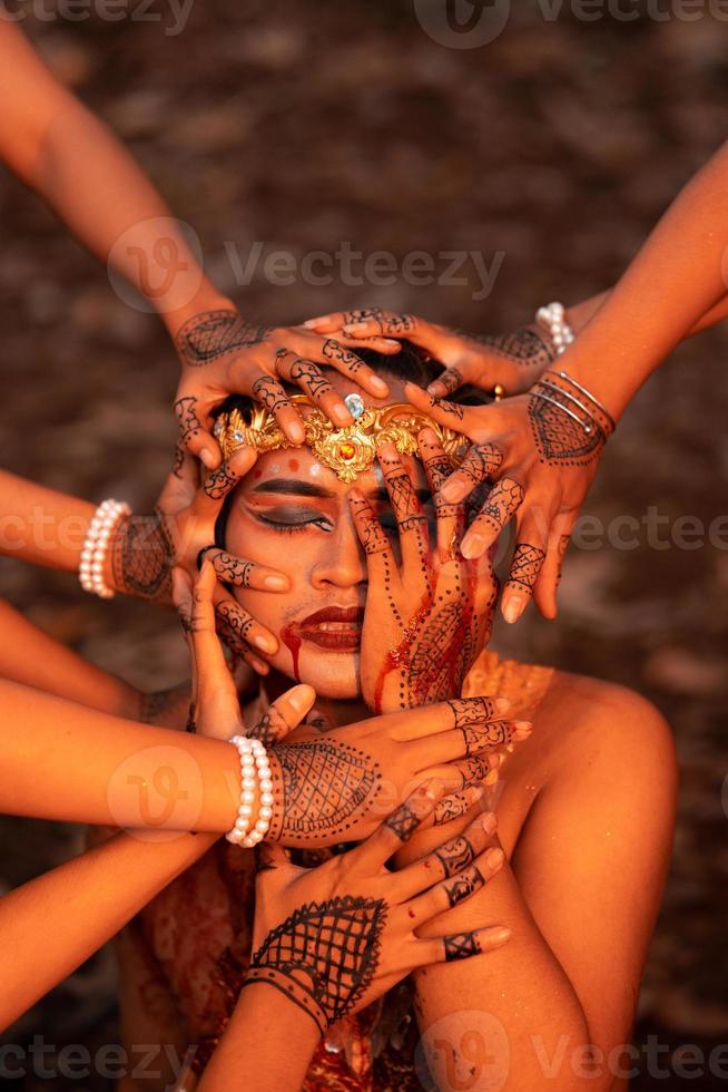 A Lot of hands holding an Asian man's face who had fake blood on her red lips like he was in pain photo