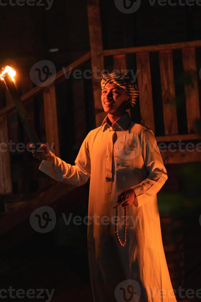 An Arabian man holding a fire torch in the front of a wooden house photo