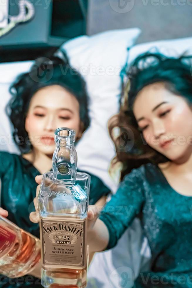 Asian women holding an alcohol bottle in their hand in the bedroom photo