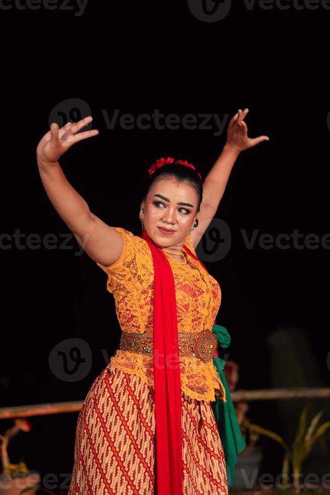 Balinese woman in traditional orange dress dancing with a red scarf while performing dancing photo