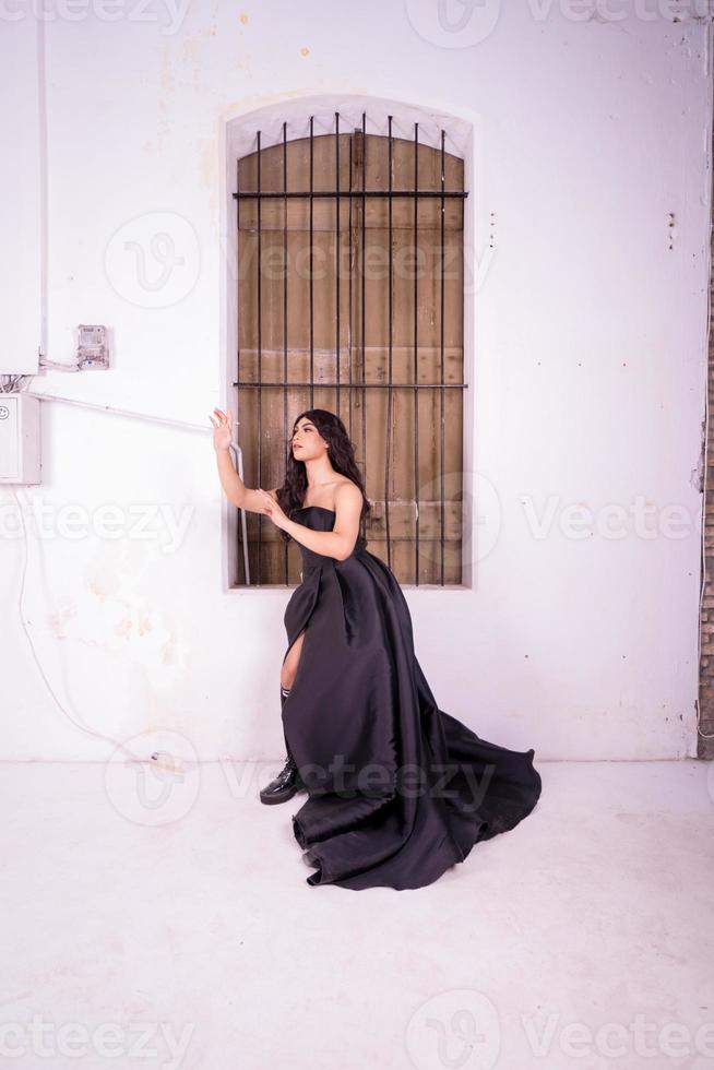 triste mujer asiática parada frente a la ventana de madera marrón mientras usa un vestido negro foto