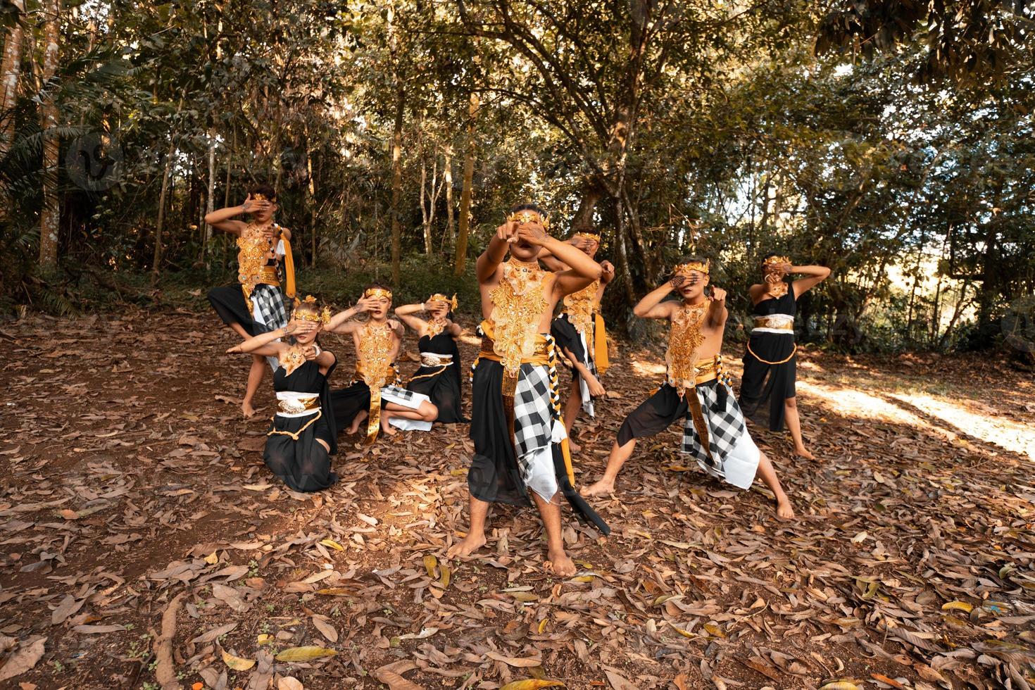 Balinese dancers with golden costumes and stripped pants dance together with the dead brown leaves in the yard photo