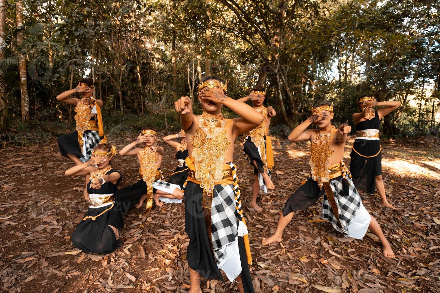 Balinese dancers with golden costumes and stripped pants dance together with the dead brown leaves in the yard photo