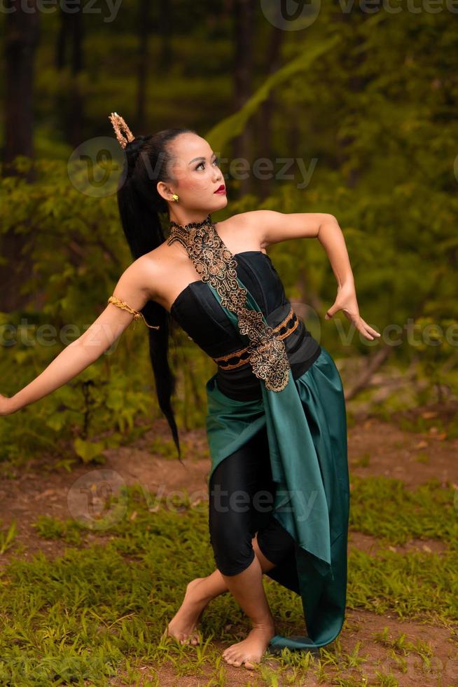 Indonesian woman with long black hair wearing a green costume with makeup in front of the forest photo