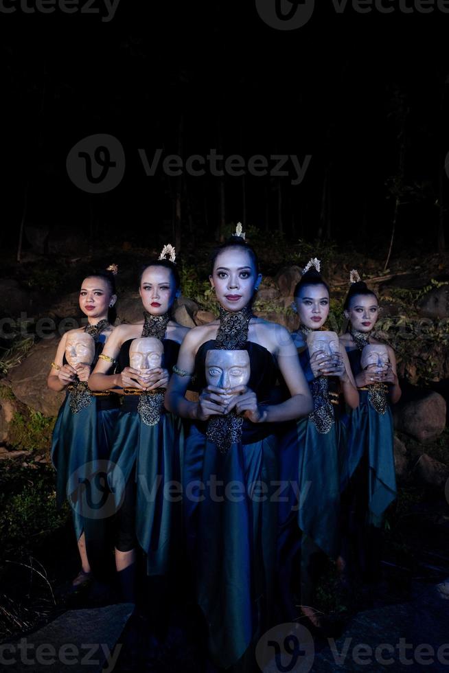 un grupo de mujeres balinesas se alinean con la máscara de madera en sus manos mientras usan trajes de baile tradicionales foto