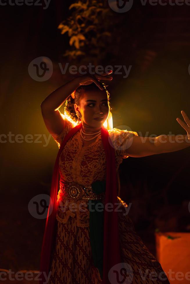 A Silhouette body of a Balinese woman in a traditional orange dress while dancing in front of the lighting on the dark night photo