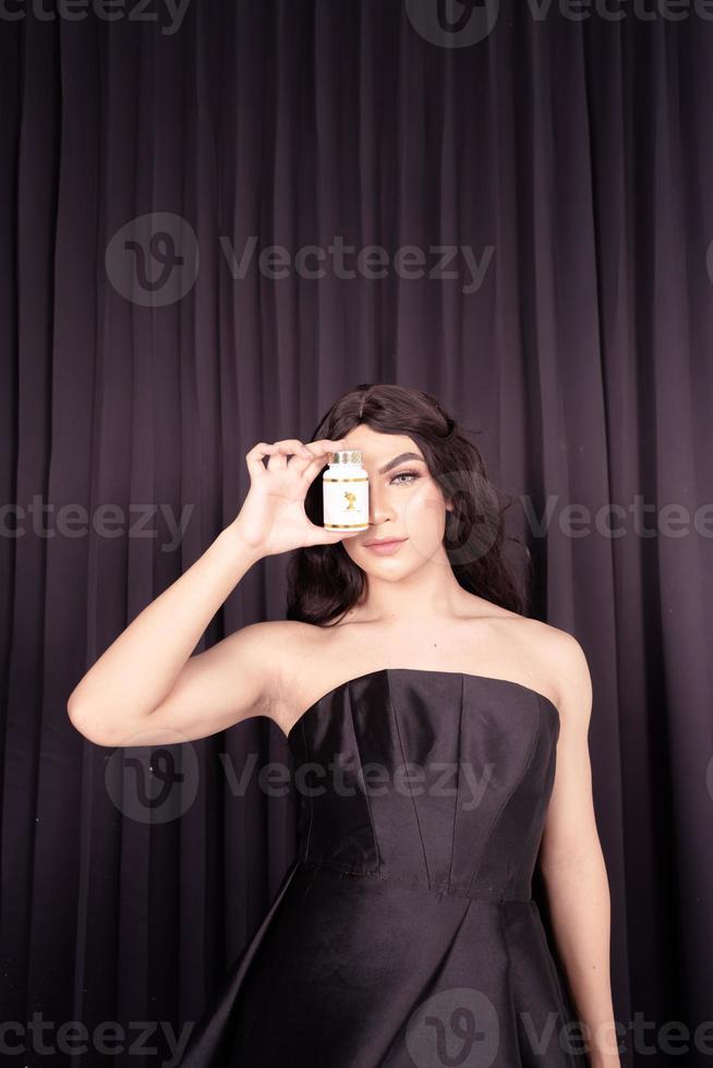 Beautiful Asian woman holding a white jar in a black dress and a black curtain photo