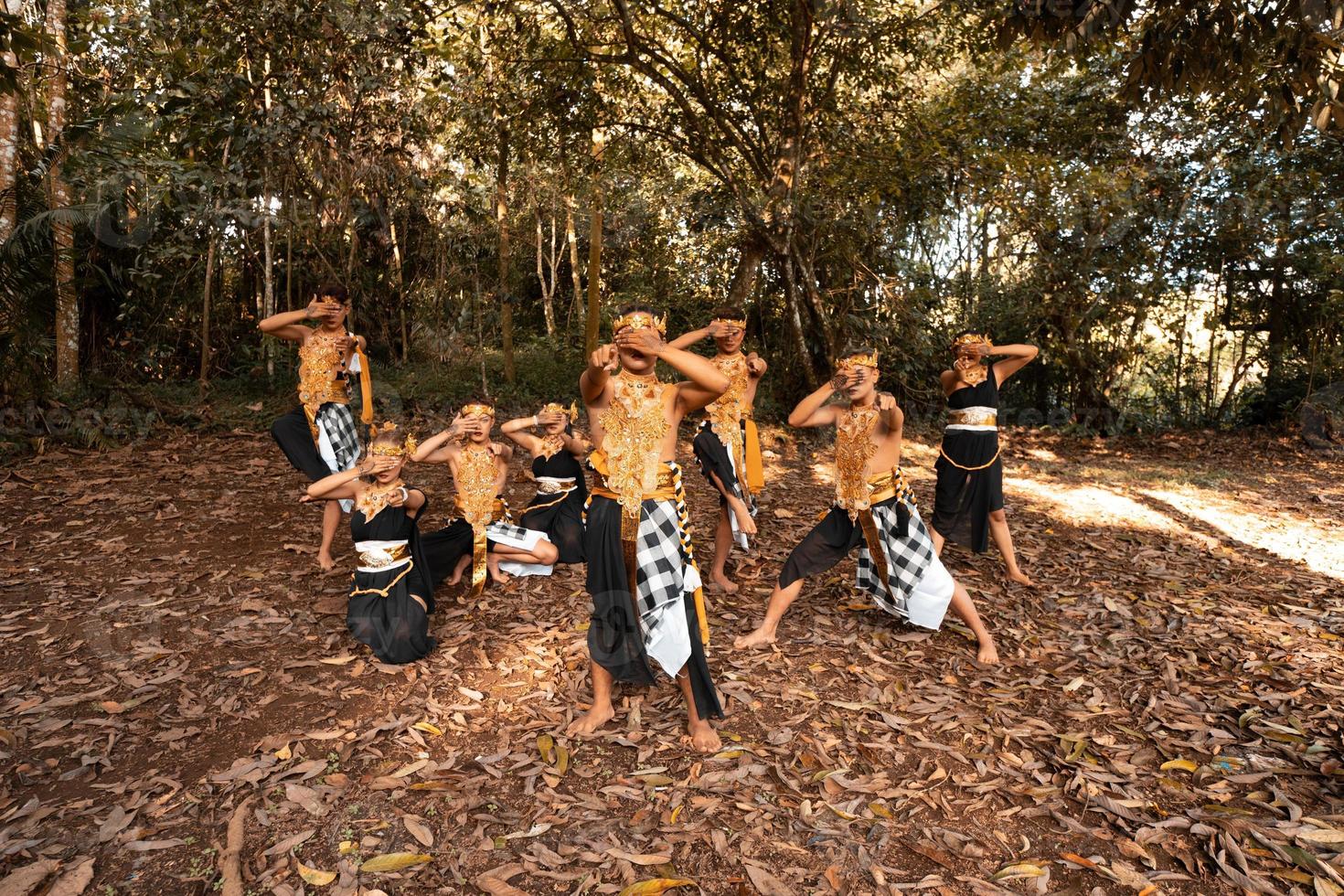 Balinese dancers with golden costumes and stripped pants dance together with the dead brown leaves in the yard photo