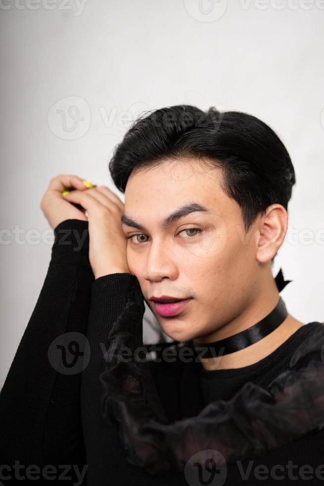 Pretty Asian man putting his hand and head on the chair while posing in a black dress photo