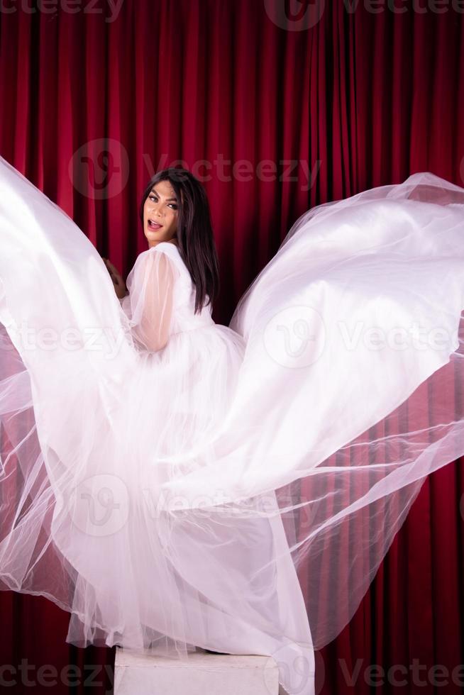 hermosa mujer asiática parada en un vestido de novia volador frente al fondo rojo foto