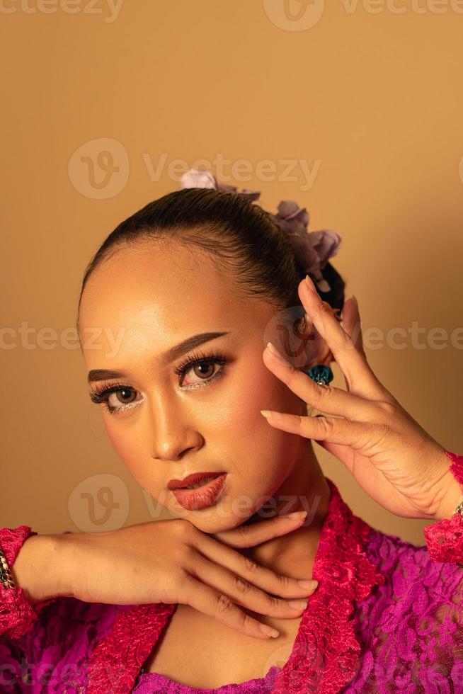 Portrait of Balinese woman with pink dress pose with hands on the face photo